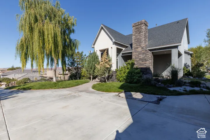 Exterior facade featuring stone veneer chimney, covered entryway, and asphalt shingle roof, complemented by established landscaping and paved driveway