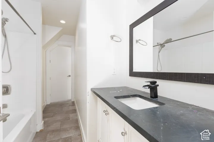 Bathroom featuring a dark-toned stone countertop, white cabinetry with silver-tone hardware, a rectangular undermount sink with a matte black faucet, and large-format rectangular floor tiling