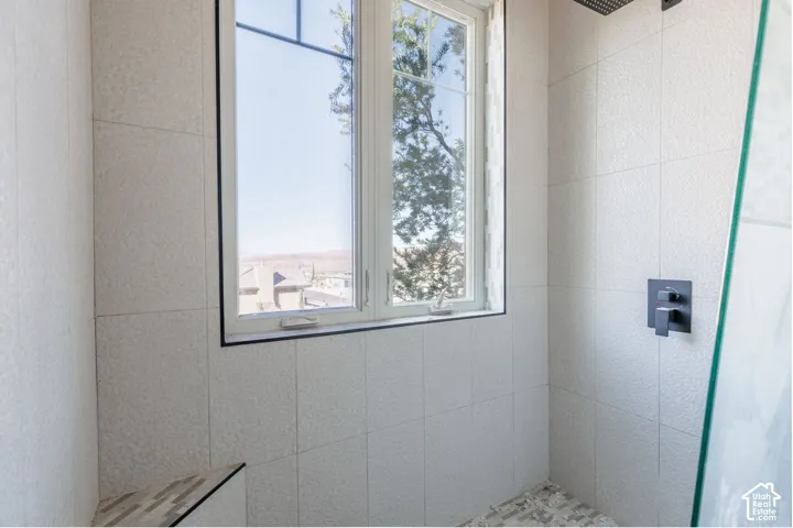 Shower stall featuring large-format textured wall tile, glass enclosure, built-in tiled bench, matte black shower hardware, and exterior exposure