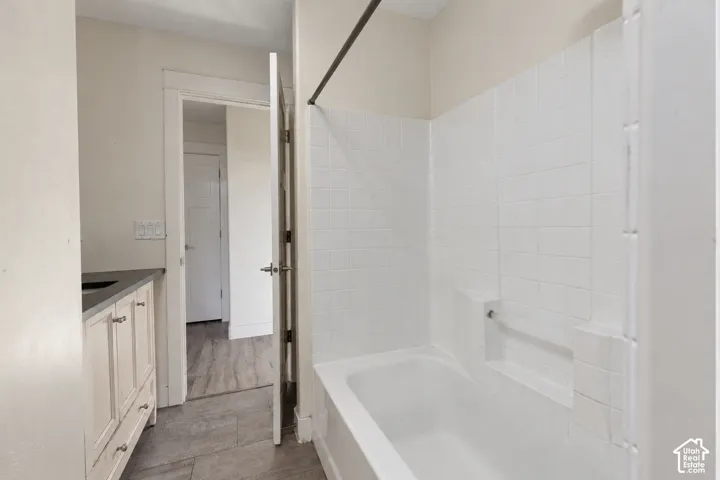 Bathroom featuring a vanity with neutral-toned cabinetry, a solid surface countertop, white tiled tub surround with integrated shelving, and wood-finish flooring