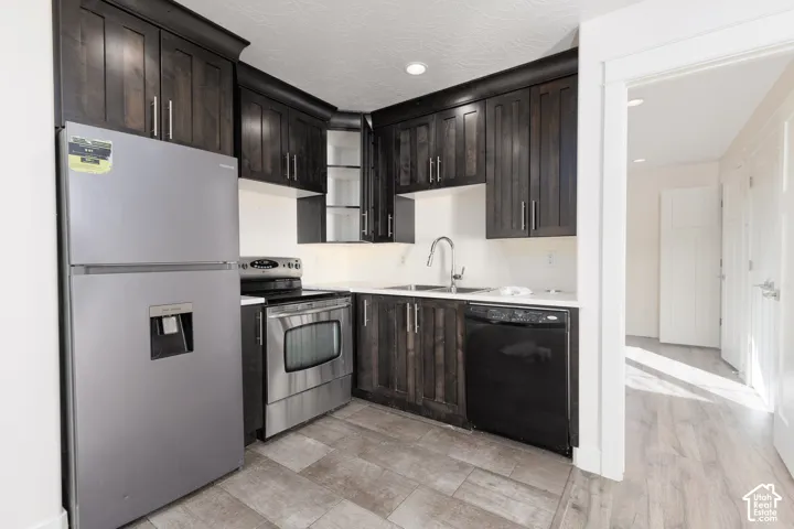Kitchen featuring dark-stained cabinetry, stainless steel appliances, light-toned solid surface countertops, a double-basin stainless steel sink with a high-arch faucet, and wood-finish flooring