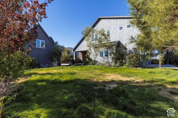 Exterior featuring a gray stucco facade, multi-gabled roofline, stone masonry accents, and multi-pane windows, set on a residential lot with mature trees