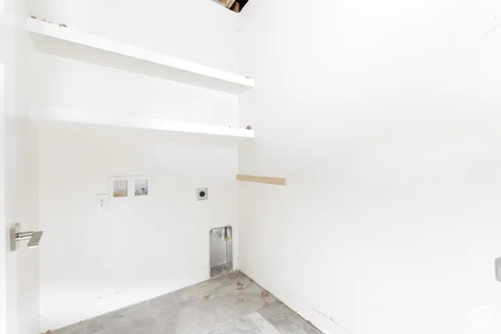 Utility space featuring matte-finish stone flooring, built-in wall shelving, and integrated plumbing and electrical hookups