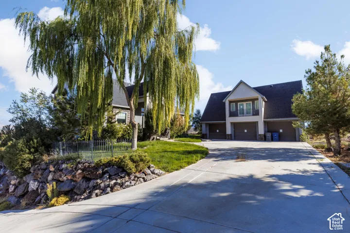 Exterior featuring a multi-car garage, upper-level balcony, stone retaining wall, and concrete driveway