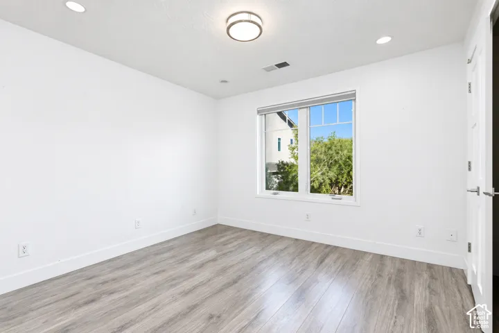 Room featuring wood-finish flooring, neutral walls, recessed lighting, a central flush-mount fixture, and a multi-pane window
