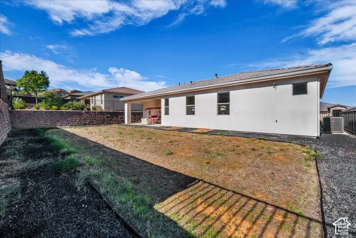 Rear exterior featuring a covered patio, neutral-tone stucco siding, a stone retaining wall, and dark gravel hardscaping