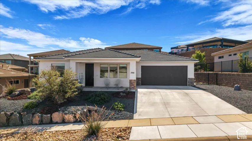 Single-story exterior featuring a hip roof, two-car garage, stone veneer accents, and xeriscaped front yard with rock retaining walls