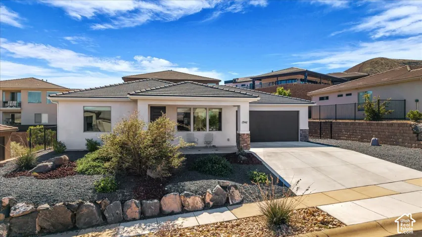 Single-story stucco exterior featuring a tiled hip roof, stone veneer accents, an attached garage, and xeriscaped front yard with rock retaining walls