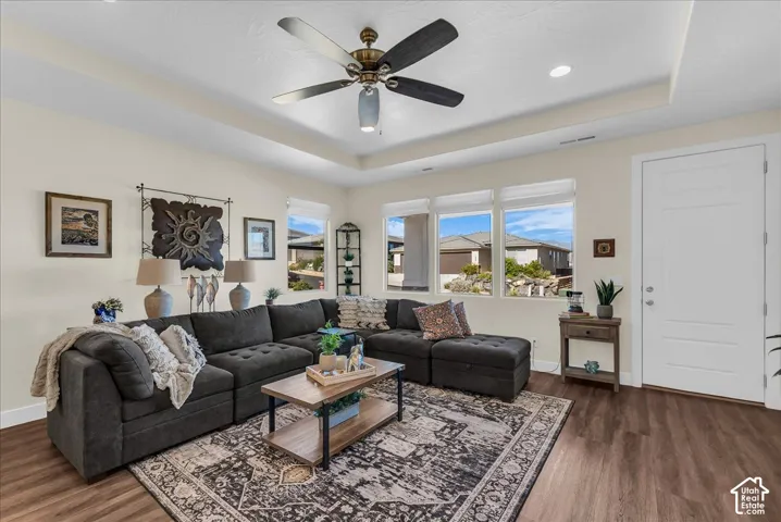 Living area featuring tray ceilings, wood-finish flooring, recessed lighting, a ceiling fan with integrated lighting, and multiple windows