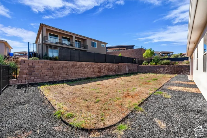 Backyard featuring tiered masonry retaining walls, black metal perimeter fencing, and decorative stone landscaping
