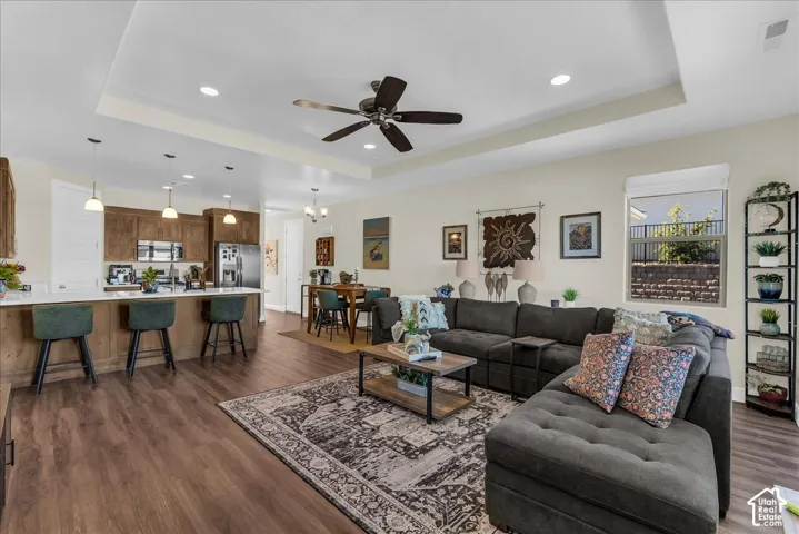 Open-concept area featuring a tray ceiling, wood-finish flooring, recessed lighting, and a kitchen island with stone-surface counters and pendant lighting