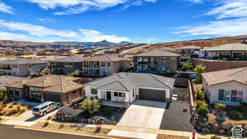 Single-level residence featuring a tile roof, two-car garage, concrete driveway, and xeriscaped front yard with a decorative rock retaining wall