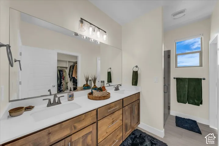 Dual-sink vanity with light-tone wood cabinetry, white solid-surface countertop, full-width wall mirror, and glass-enclosed shower