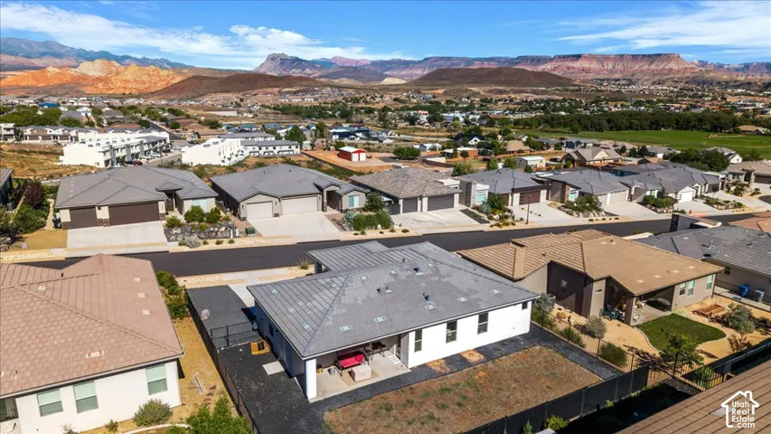 Aerial perspective of a contemporary residence featuring a pitched roof, rear covered patio, fenced backyard, and expansive desert mountain backdrop