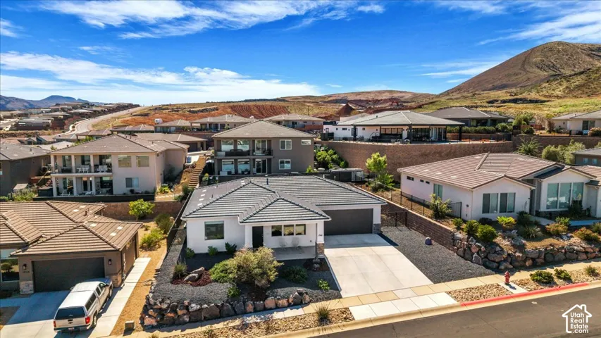 Single-story residence featuring a tile roof, light-toned exterior finish, concrete driveway, and xeriscaped front landscaping with stone retaining walls