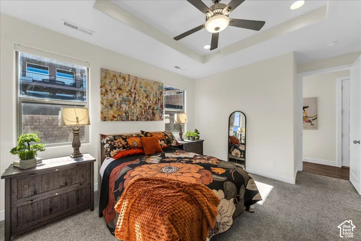 Tray ceiling featuring a central multi-blade ceiling fan with integrated lighting, dual-pane windows, and neutral carpeting