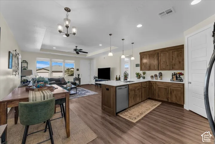 Open-concept kitchen and living area featuring a tray ceiling, recessed lighting, wood-finish flooring, a large kitchen island with countertop seating, and stained wood cabinetry