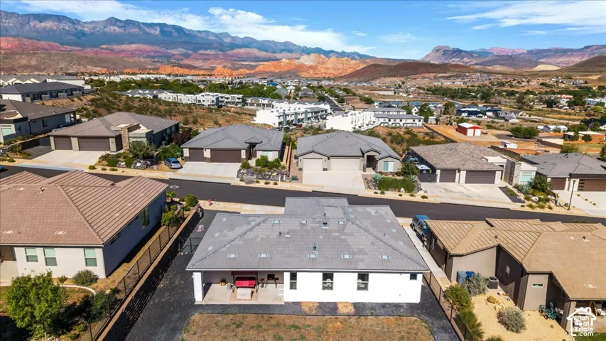 Aerial perspective of a residential property featuring a gray tile roof, a covered patio, a fenced rear yard, and a desert mountain backdrop