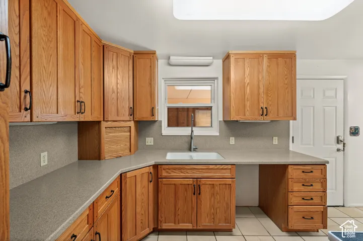Kitchen featuring stained wood cabinetry, solid surface countertops, a dual-basin undermount sink with a gooseneck faucet, tile flooring, and a built-in drawer stack