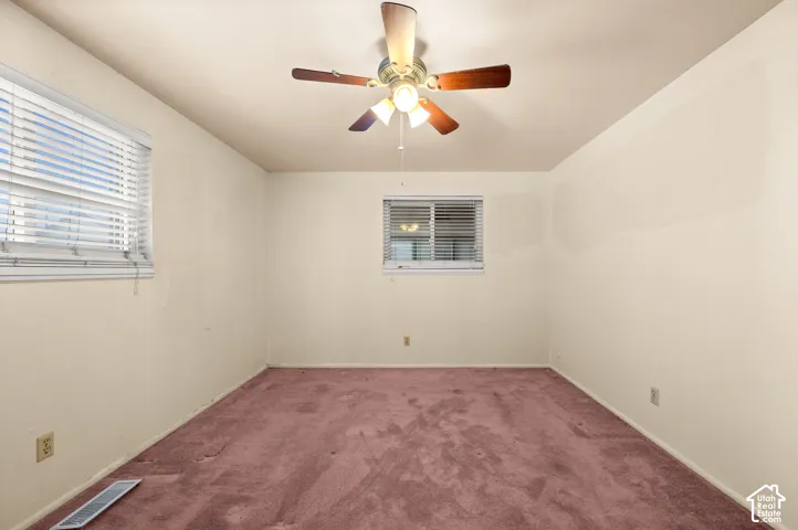Interior room featuring two windows with horizontal blinds, carpeted flooring, and a multi-blade ceiling fan with an integrated light fixture