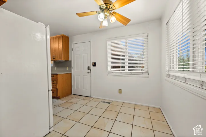 Tile flooring, ceiling-mounted light fixture with fan, wood cabinetry, and multiple windows with horizontal blinds