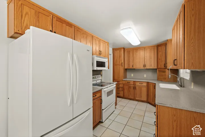 Kitchen featuring oak-finish cabinetry, solid surface countertops, white appliances, and tiled flooring