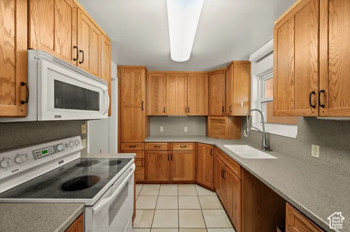 Kitchen featuring solid wood cabinetry, neutral countertops, white appliance suite, dual-handle gooseneck faucet, and tile flooring