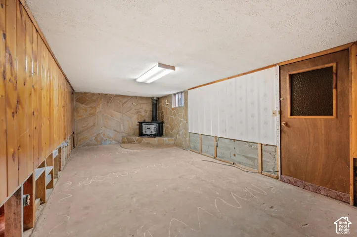 Interior space featuring stone-clad masonry walls, wood paneling, a wood-burning stove on a raised hearth, and a wooden door with a textured glass pane