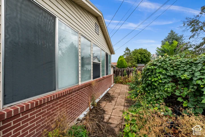 Exterior side profile featuring red brick masonry, horizontal lap siding, a row of large rectangular windows, and a paved stone walkway