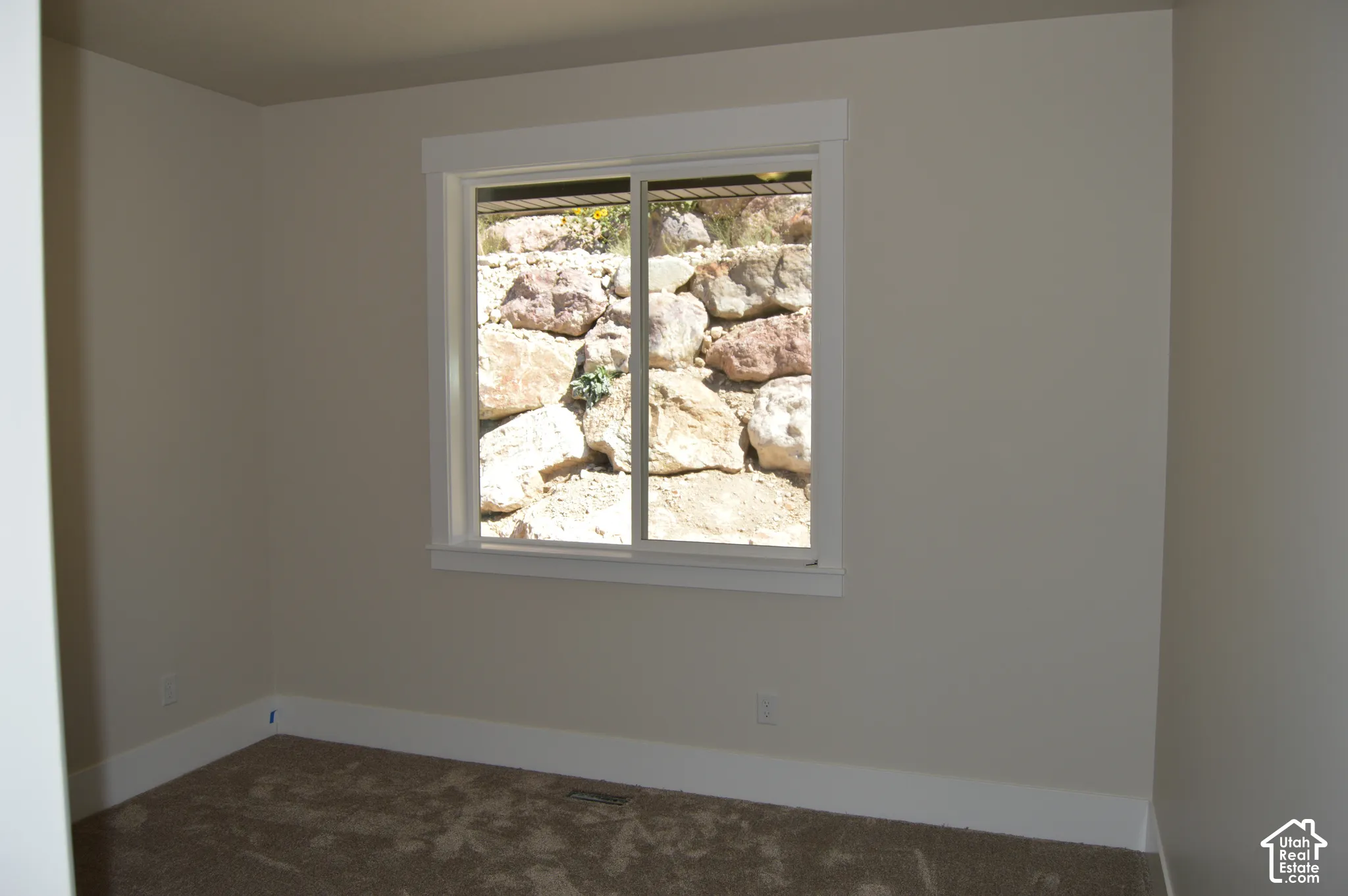 Neutral wall-to-wall carpeting, wide window casing, and sliding window featuring an exterior stone retaining wall backdrop