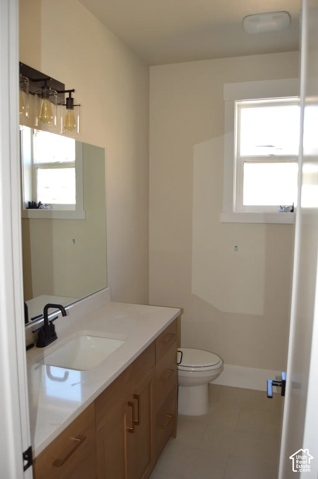 Bathroom featuring a wood-finish vanity with a stone countertop, an integrated rectangular sink, matte black hardware, and a three-light wall fixture
