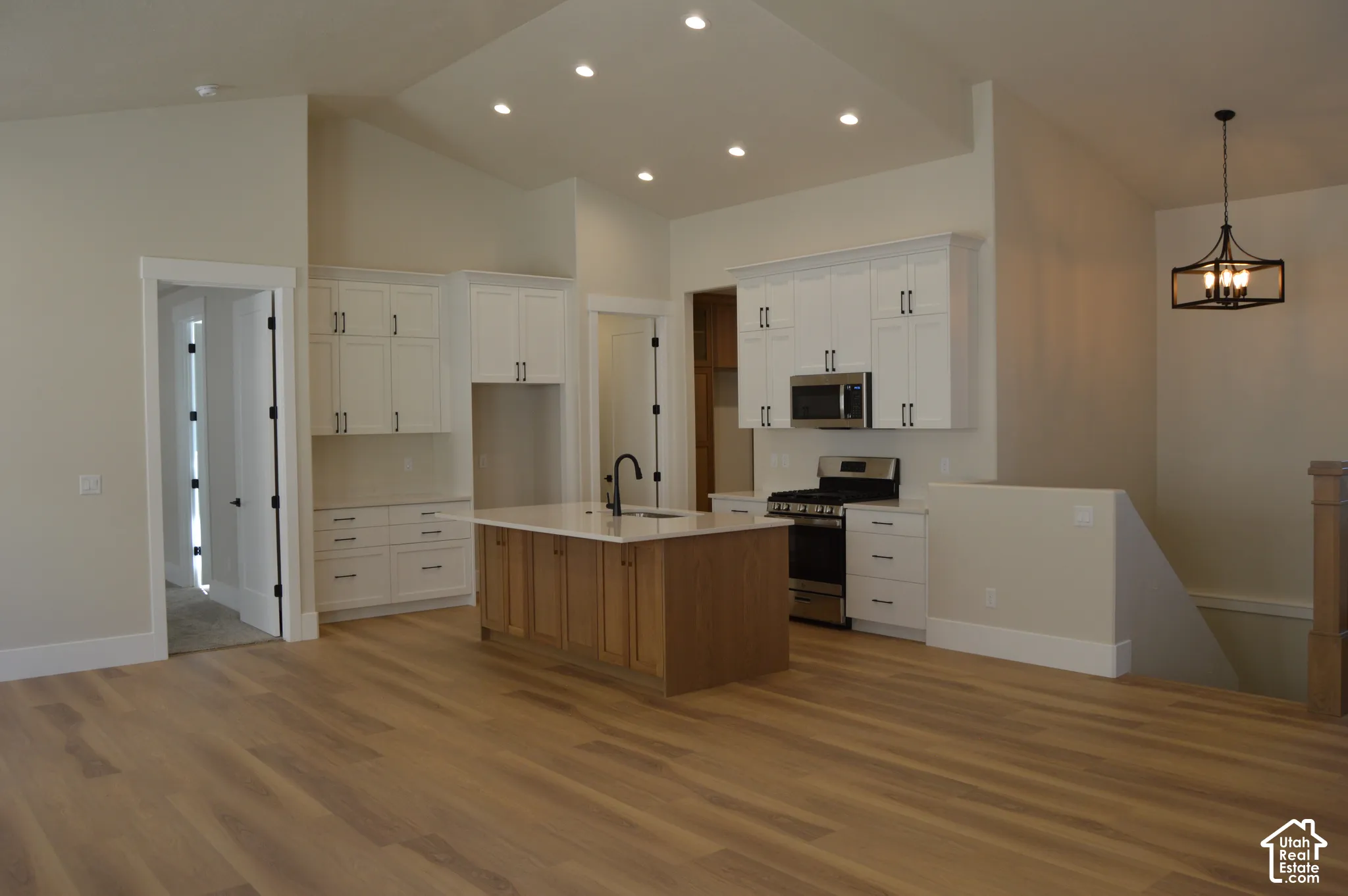 Kitchen featuring white upper and lower cabinetry, a wood-finish island with a light-toned countertop, recessed ceiling lighting, wood-finish flooring, and a metal lantern-style pendant light