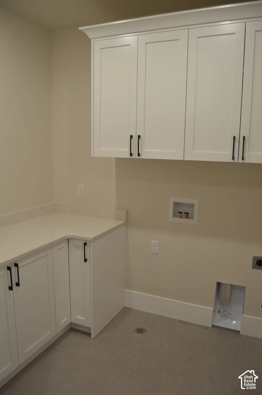 Laundry room featuring white Shaker-style cabinetry, quartz countertop, and neutral flooring