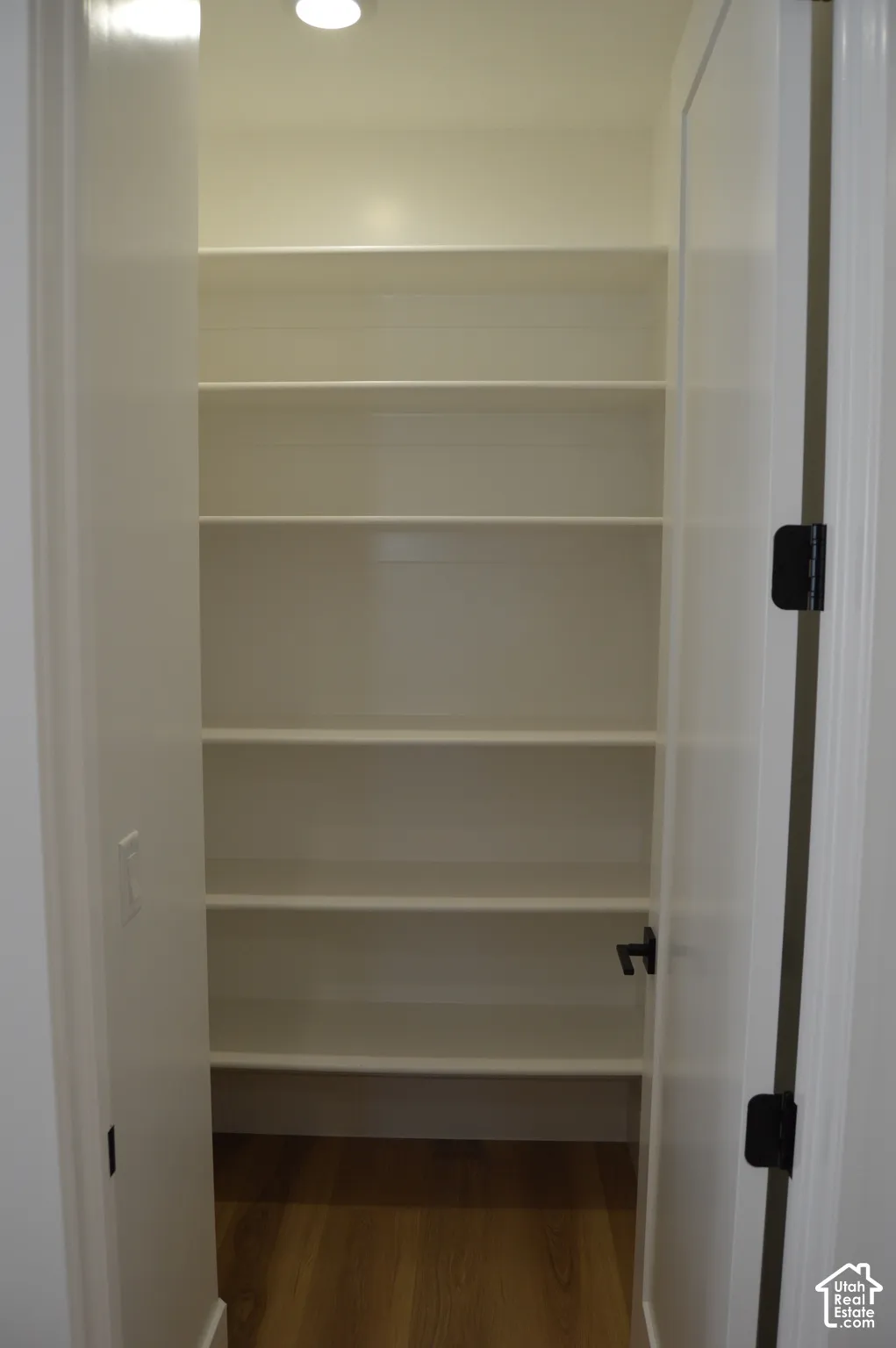 Walk-in storage space featuring five tiers of built-in shelving, wood-finish flooring, and a recessed ceiling light