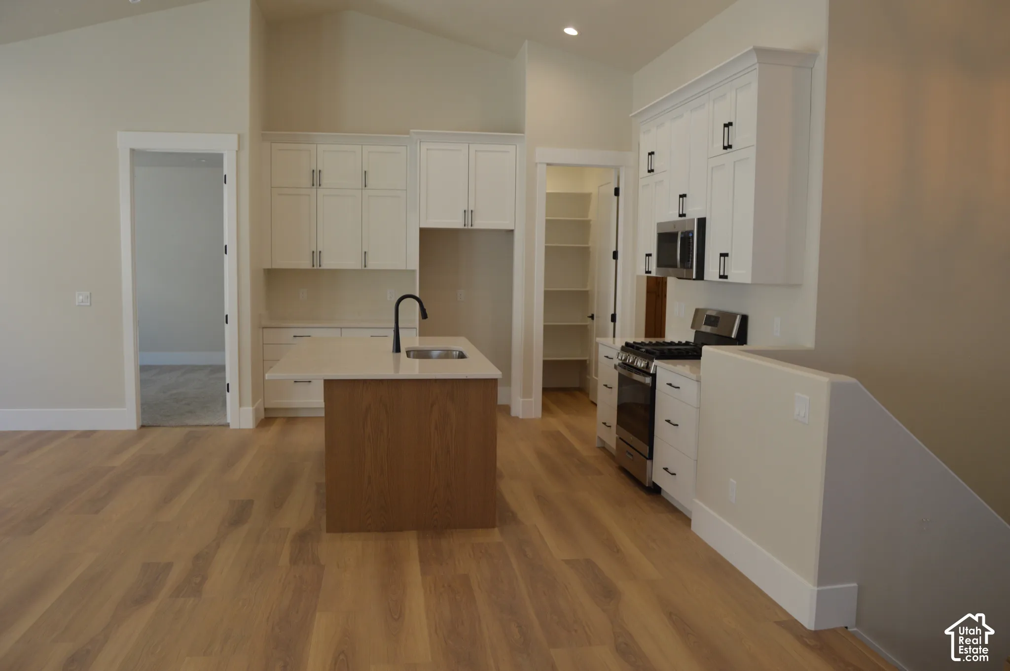 Kitchen featuring white shaker-style cabinetry, wood-finish flooring, a central island with a stone-surface countertop, stainless steel appliances, and a walk-in pantry