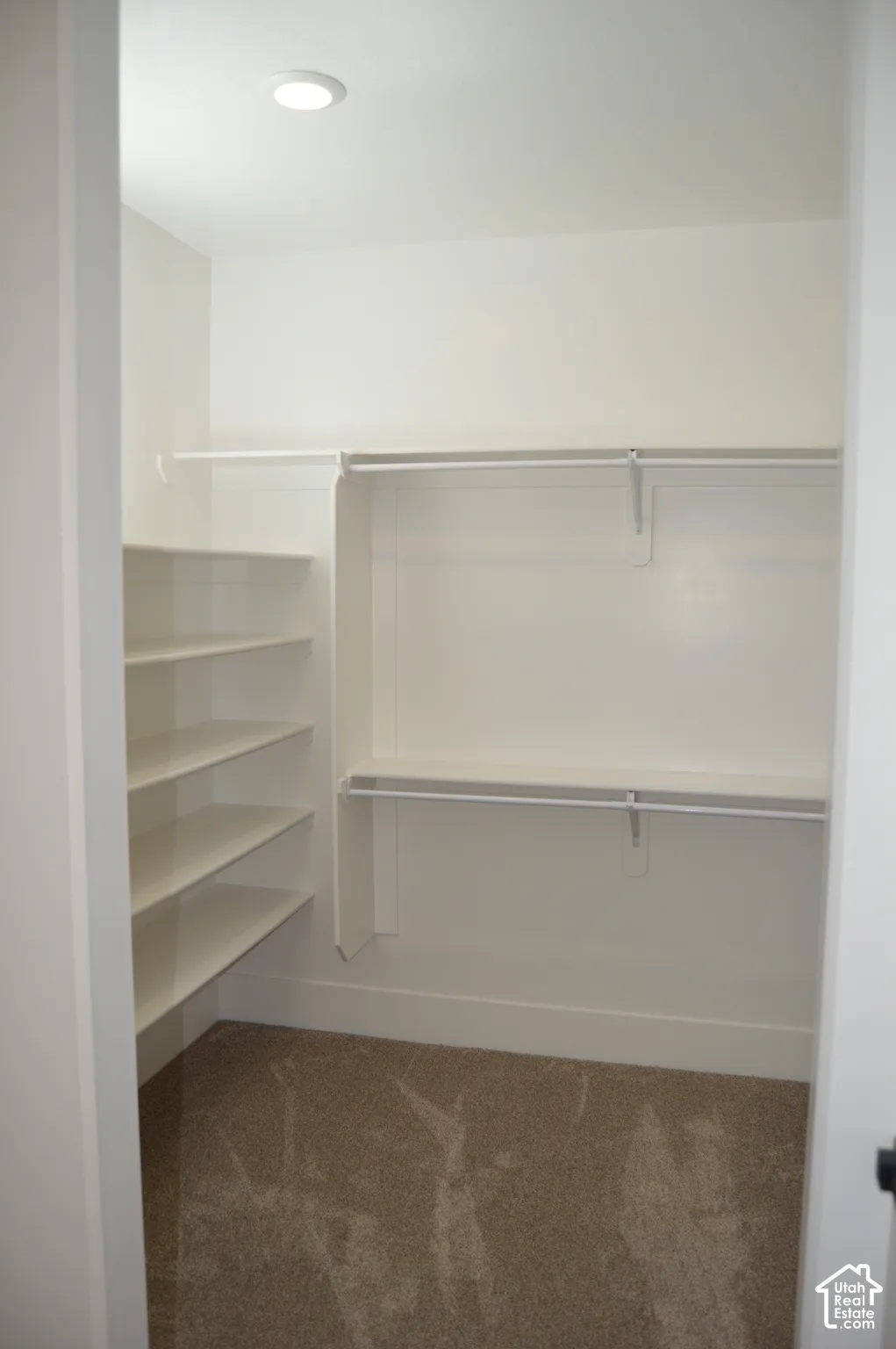 Walk-in closet featuring wall-to-wall carpeting, white shelving units, a built-in tiered storage system, dual hanging rods, and recessed lighting
