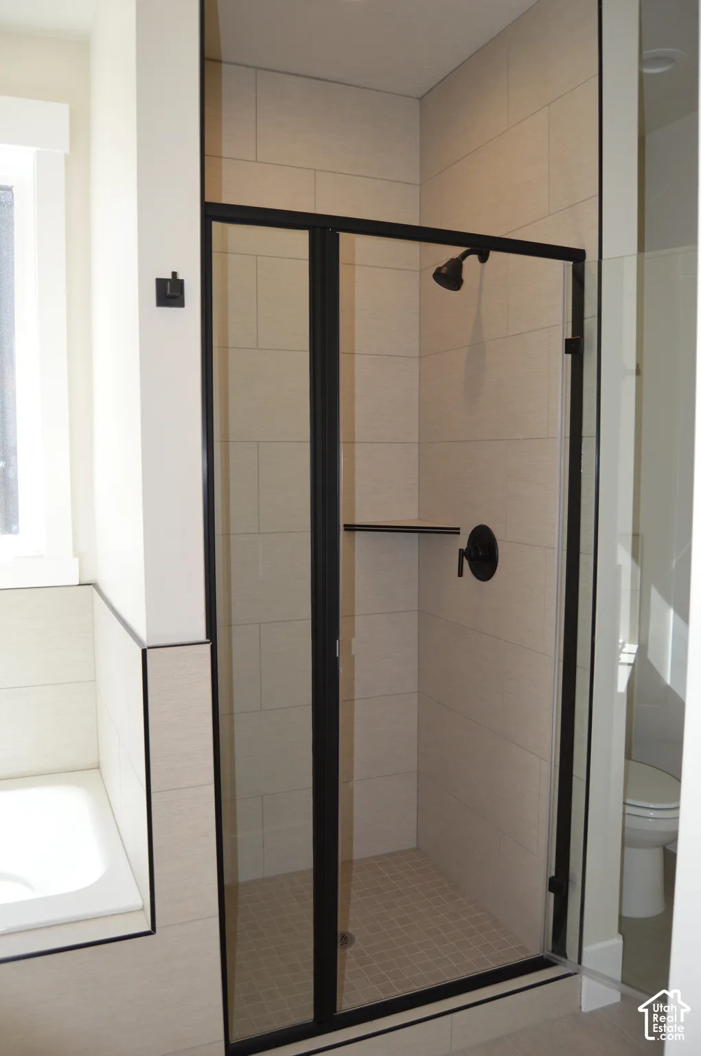 Walk-in shower featuring a matte black frame, glass door, floor-to-ceiling tile surround, built-in corner shelving, and matte black plumbing fixtures
