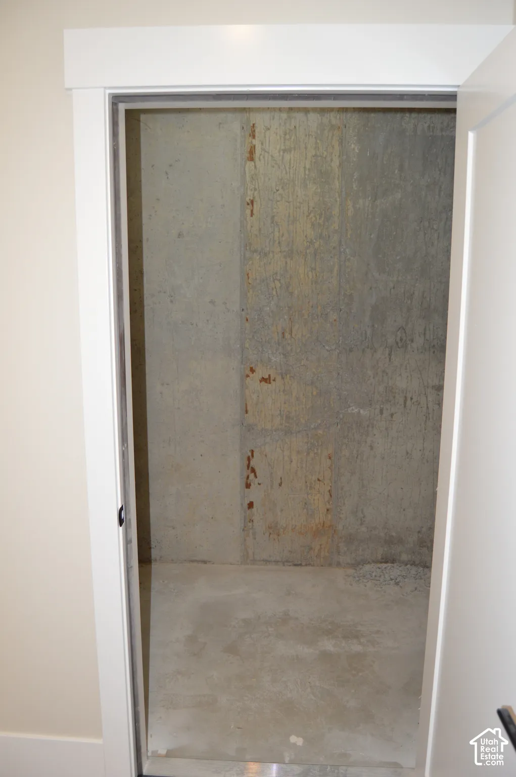 Storage space featuring poured concrete walls and a concrete floor, accessed by a white interior door with minimalist door casing