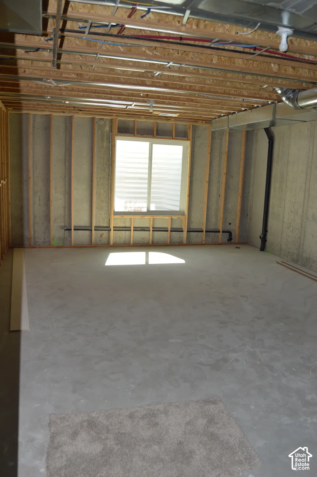 Unfinished interior space featuring exposed wood-stud framing, concrete flooring, and a single window with an external egress window well