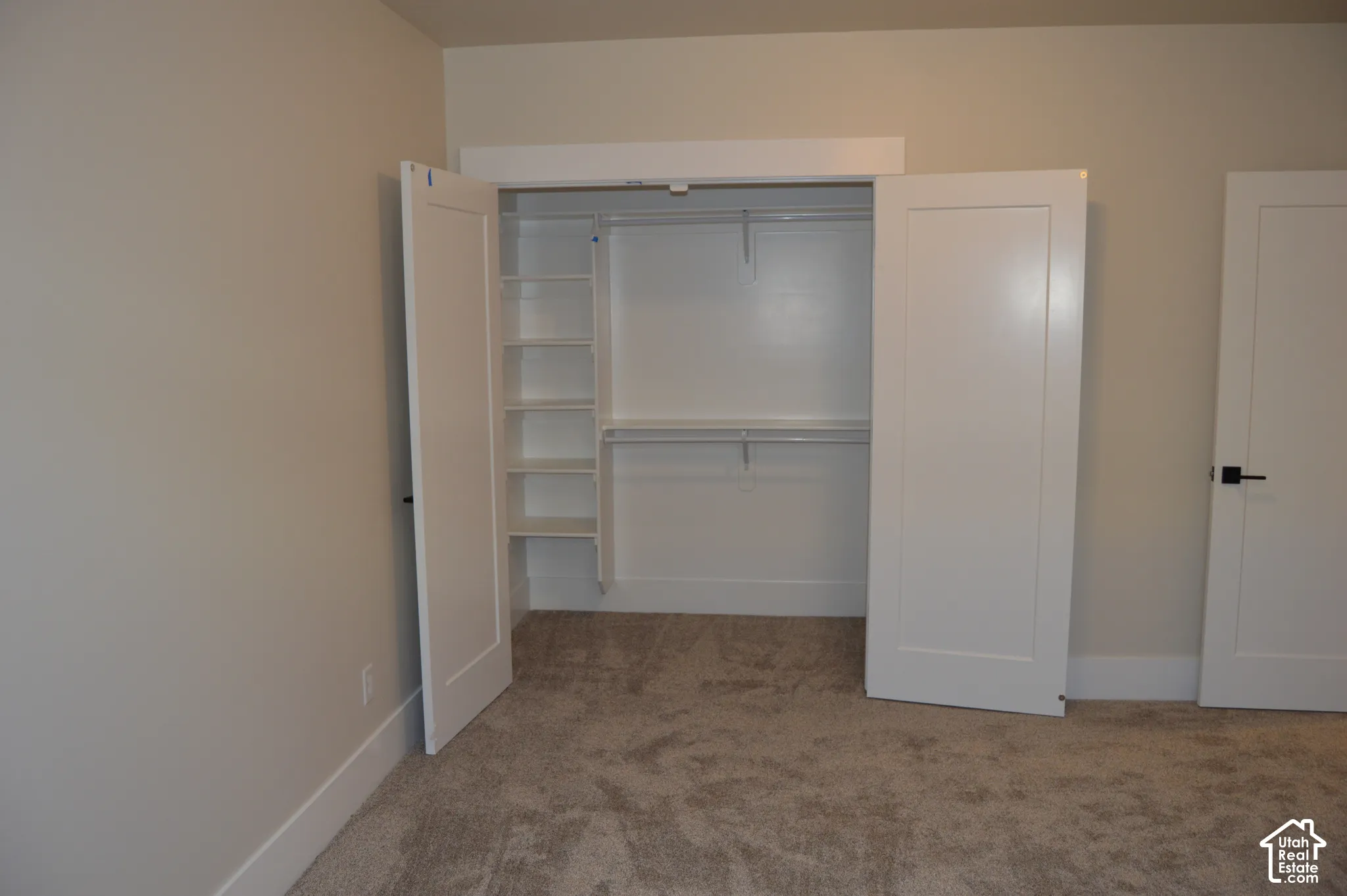 Closet featuring white shaker-style doors, built-in shelving, and hanging rods, paired with neutral carpeting
