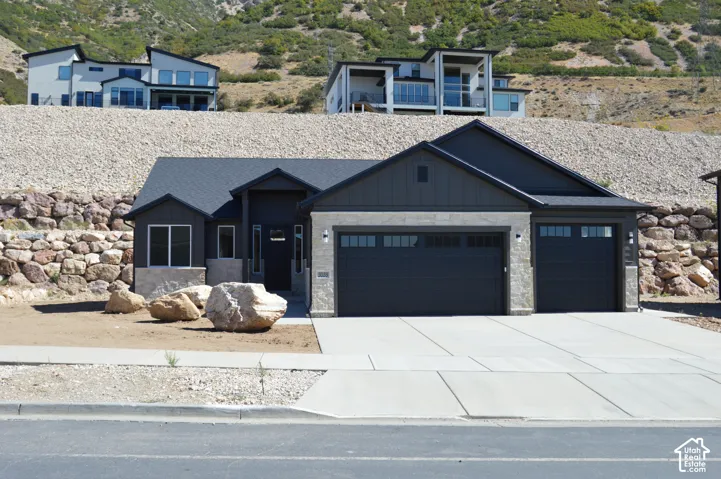 Modern exterior featuring dark vertical siding, stacked stone veneer, a three-car garage, and concrete driveway