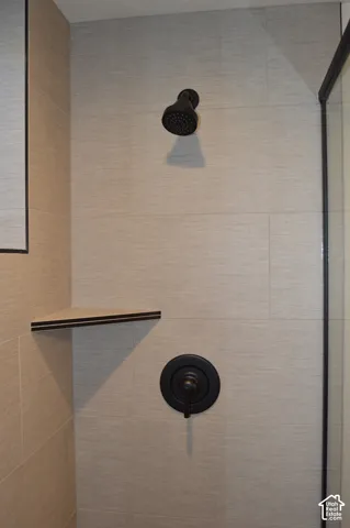 Shower stall featuring large-format neutral-toned wall tiles, matte black shower head and control valve, integrated corner shelving, and a glass enclosure