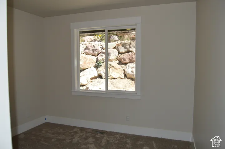 Neutral wall-to-wall carpeting, wide window casing, and sliding window featuring an exterior stone retaining wall backdrop