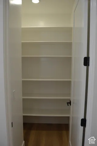 Walk-in storage space featuring five tiers of built-in shelving, wood-finish flooring, and a recessed ceiling light