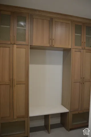 Custom wood-finish cabinetry featuring integrated shelving, light-toned stone-surface bench seating, vertical metallic hardware, and upper cabinet doors with decorative metal mesh inserts