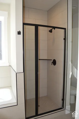Walk-in shower featuring a matte black frame, glass door, floor-to-ceiling tile surround, built-in corner shelving, and matte black plumbing fixtures