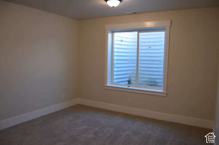 Room featuring neutral wall tones, wall-to-wall carpeting, an egress window with a corrugated metal window well, and a flush-mount ceiling light fixture
