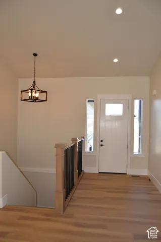 Entryway featuring wood-finish flooring, recessed lighting, a geometric metal pendant fixture, and a single-panel door with sidelights and wood-post railing