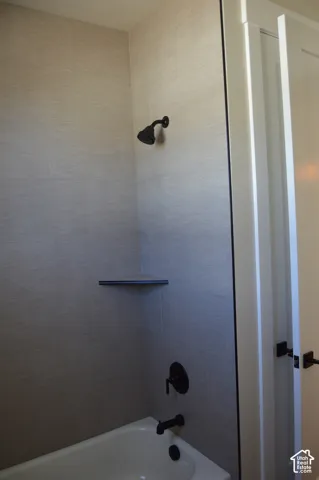 Shower and tub combination featuring textured tile surround, built-in corner shelving, and matte black plumbing fixtures