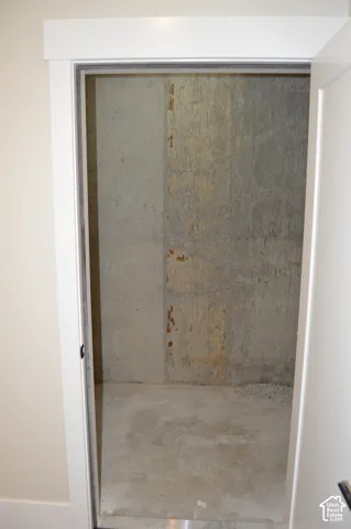 Storage space featuring poured concrete walls and a concrete floor, accessed by a white interior door with minimalist door casing